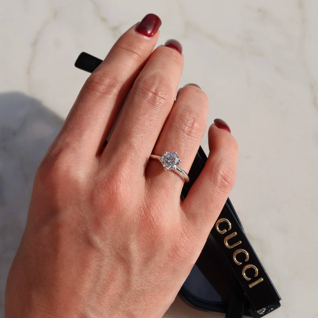 Hand with solitaire lab-grown diamond ring and Gucci sunglasses on marble surface