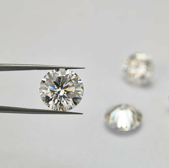 Round lab-grown diamond held by tweezers with loose diamonds on a light background