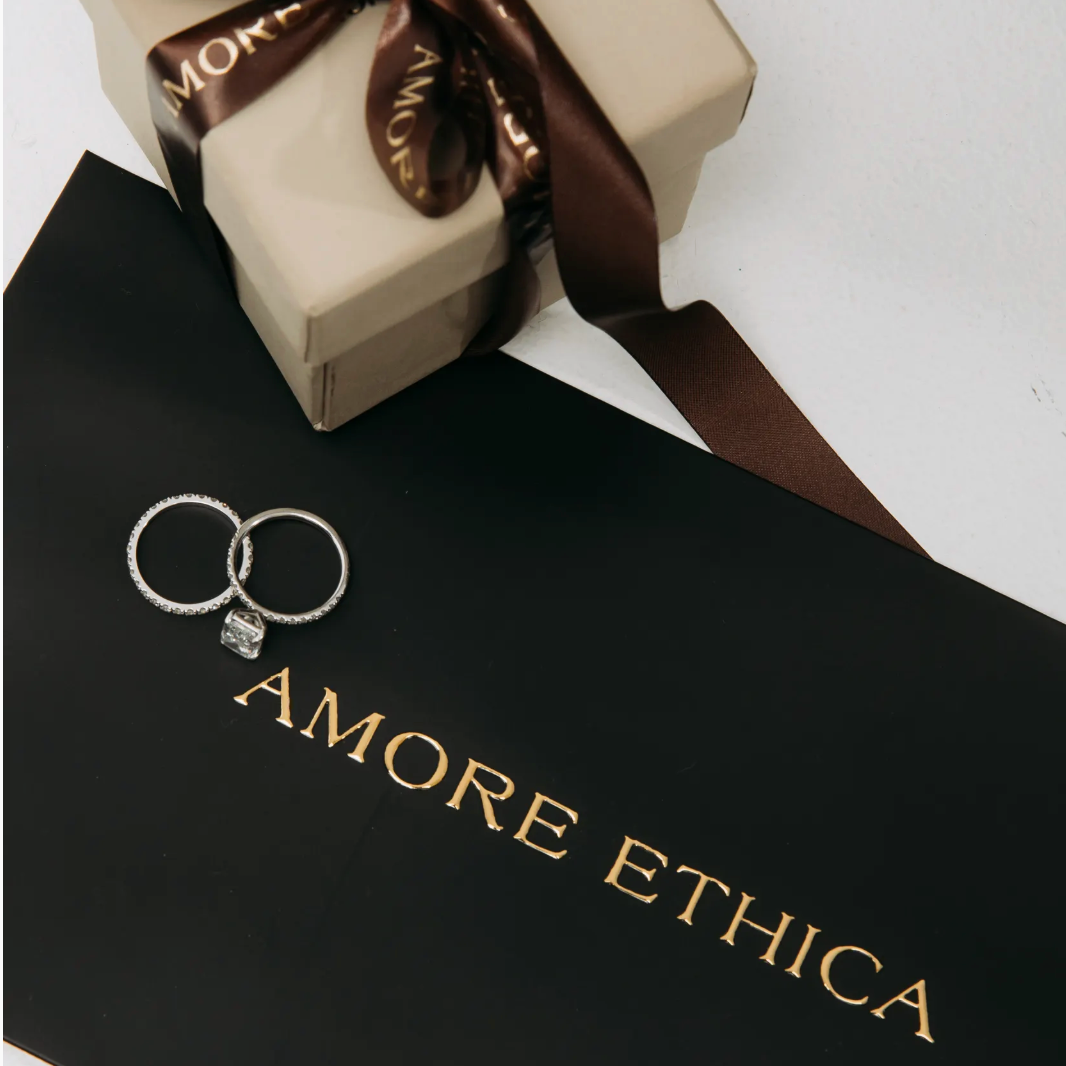 Lab-grown diamond engagement rings on black gift box with gold lettering and brown ribbon