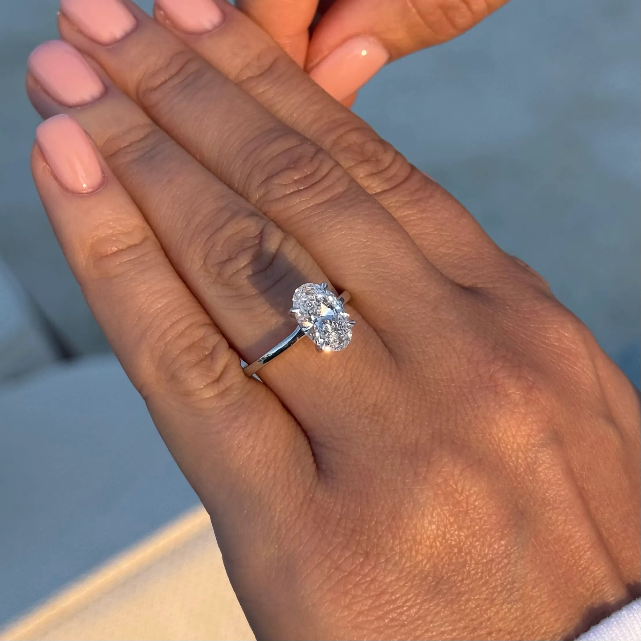 Oval lab-grown diamond engagement ring on woman's hand with manicured nails in natural light