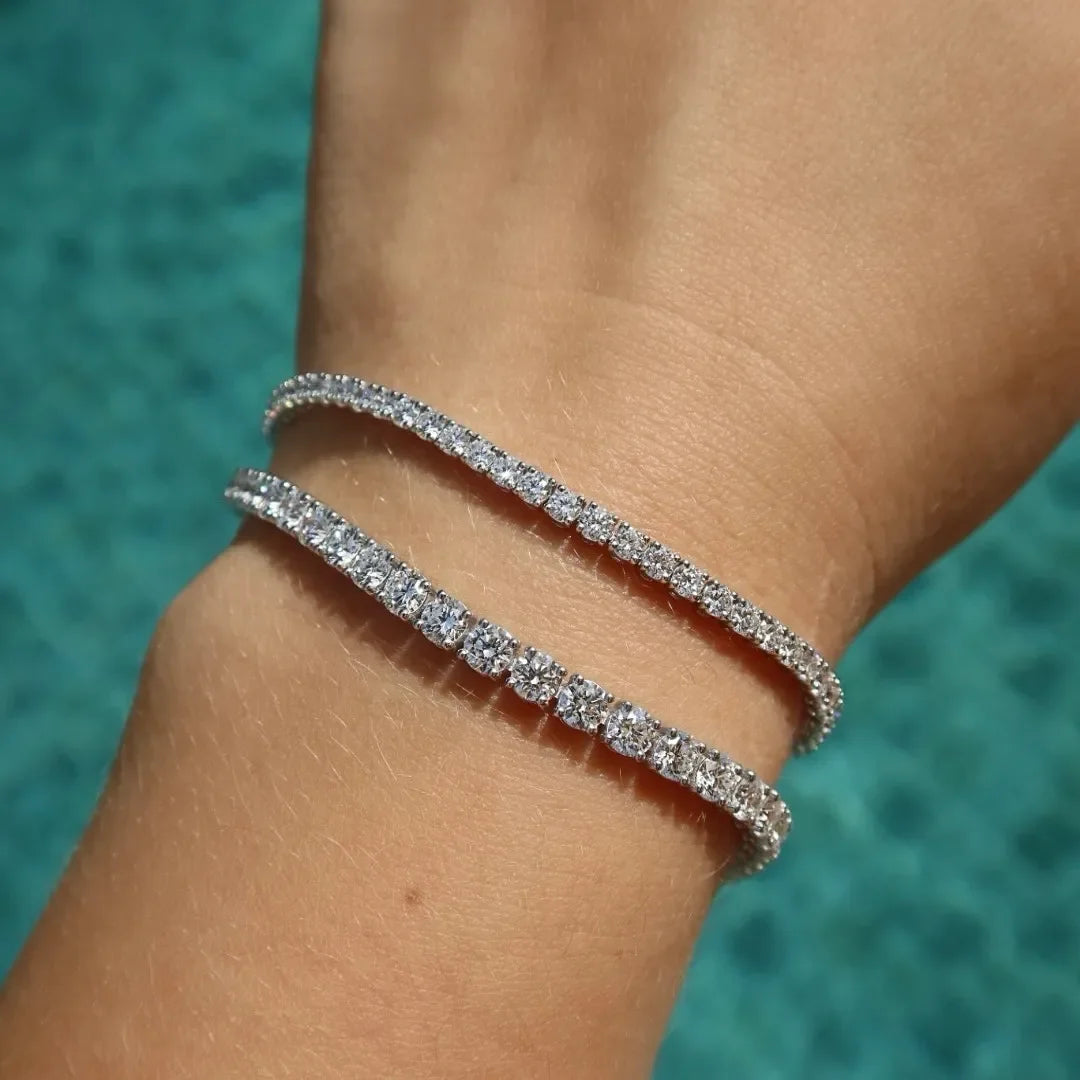 Two lab-grown diamond tennis bracelets on wrist with sparkling stones by a blue background
