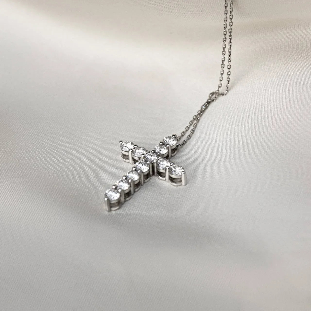 Lab-grown diamond cross pendant necklace on a silver chain resting on ivory fabric