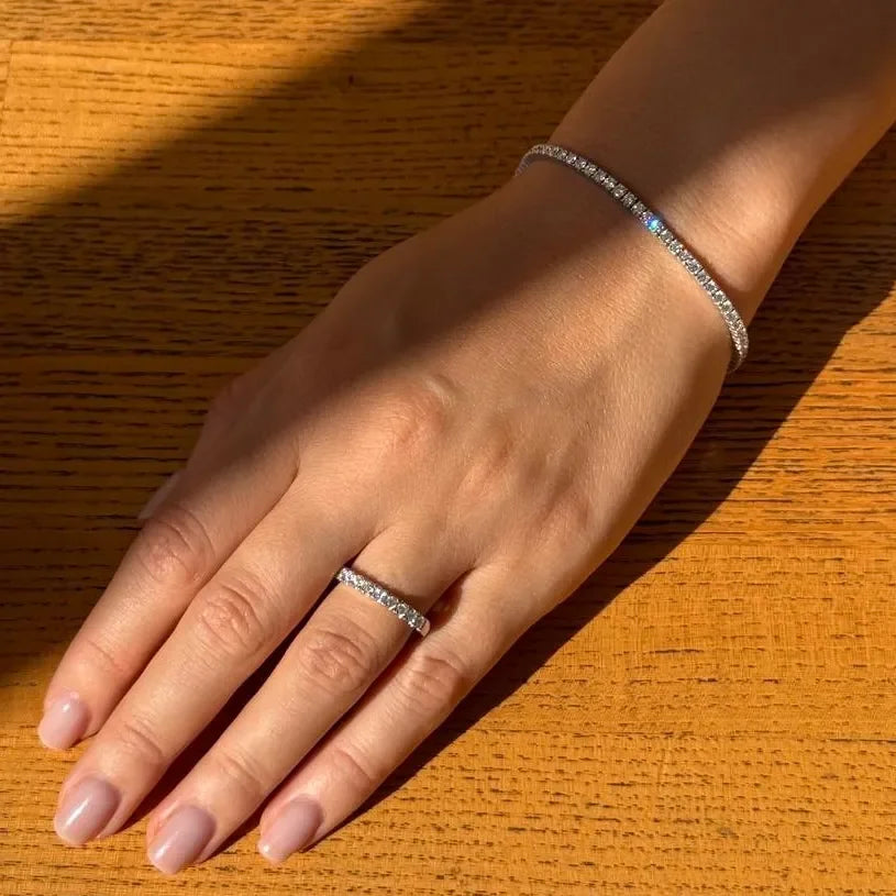 Hand wearing lab-grown diamond tennis bracelet and eternity ring on wood table