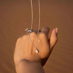 Hand holding a delicate pear-shaped lab-grown diamond pendant necklace and pearl ring